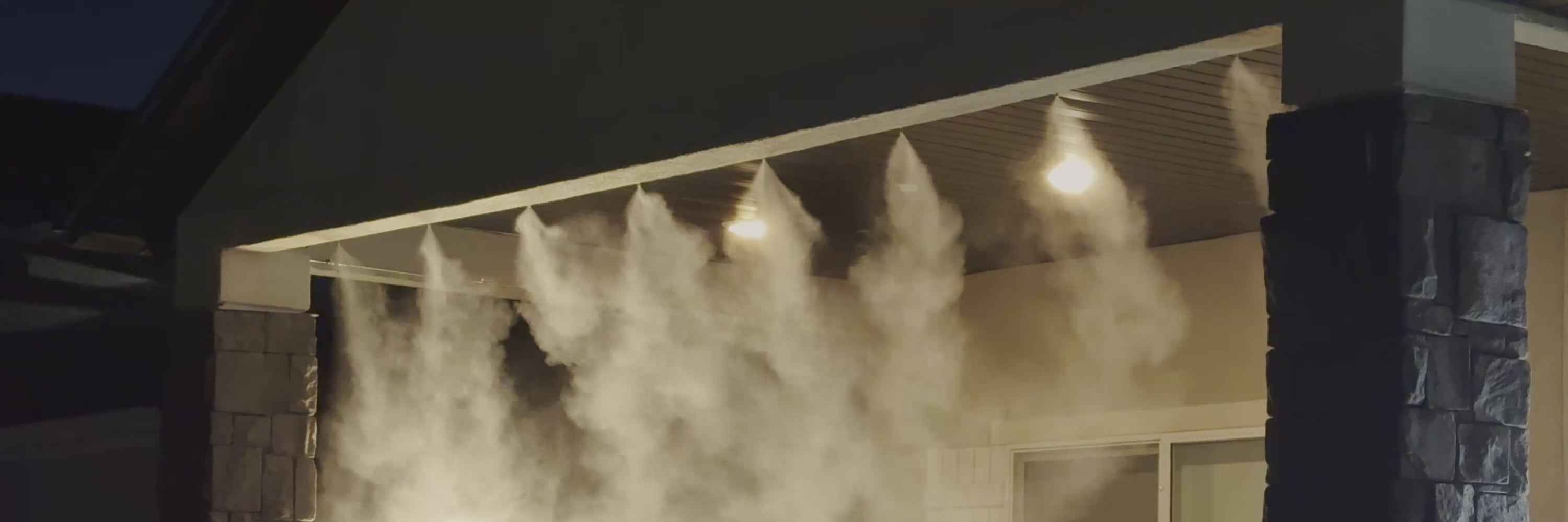 Load video: A high pressure misting system on a patio in the evening with fine atomization small enough to appear more like fog. 